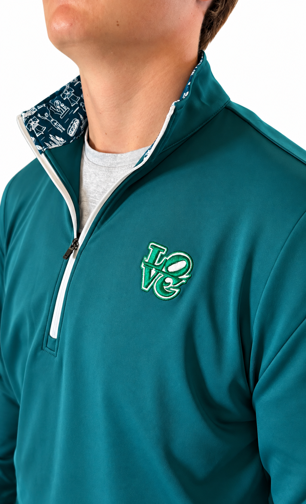 The Philly Heritage Zip Up teal quarter-zip pullover with a white zipper, patterned collar lining, and green chest emblem.
