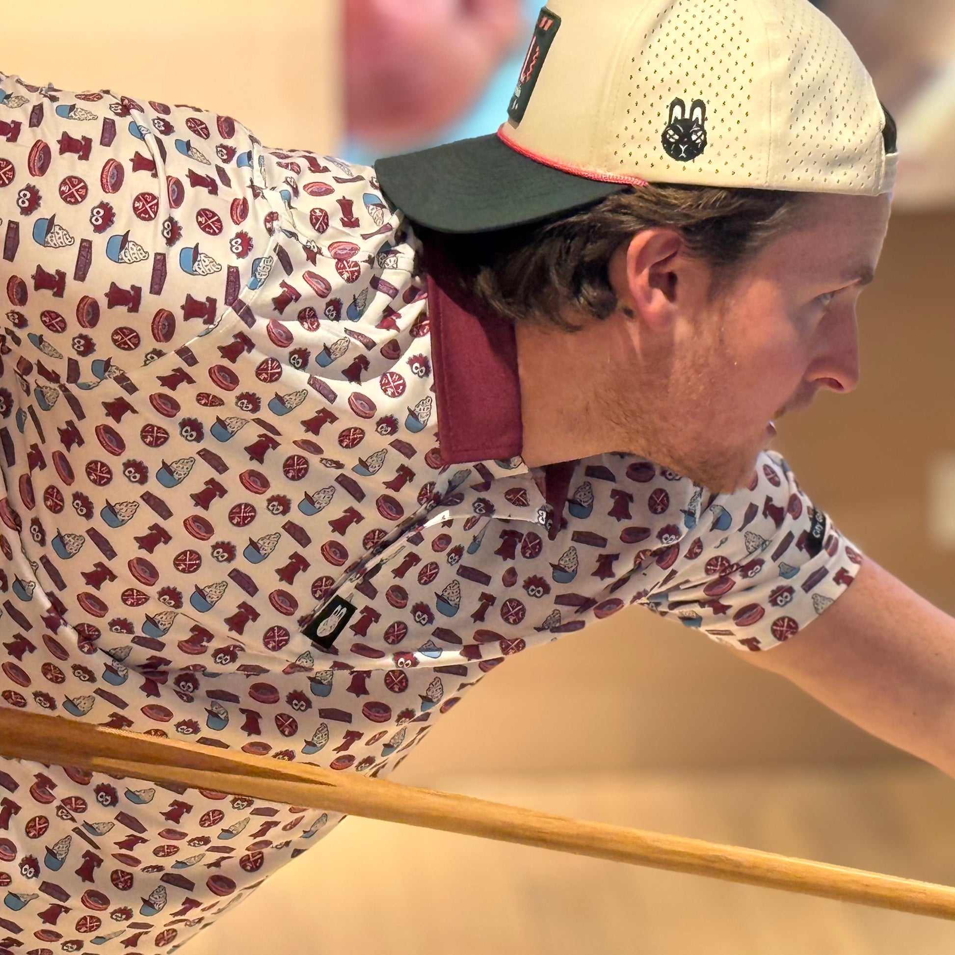 The Pattison Classic Phillies-inspired golf polo worn by man playing billiards, retro baseball pattern performance shirt by City Golf Collective