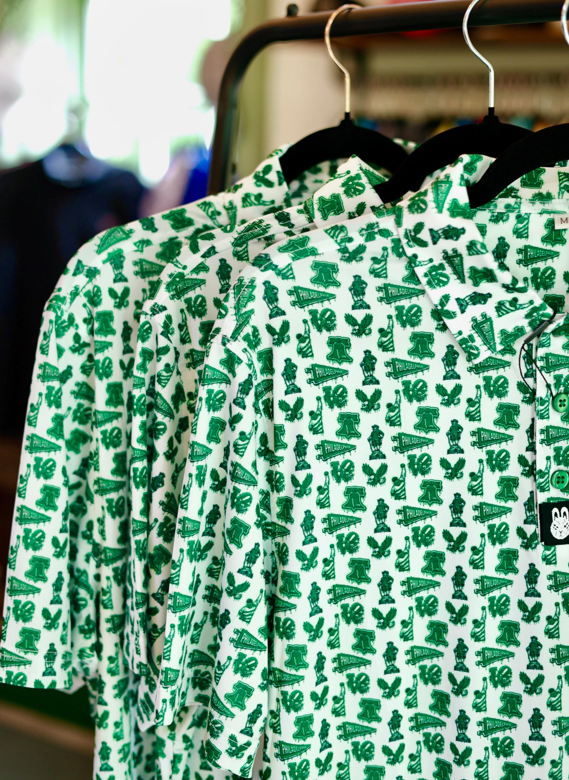 Bleeding Green Polo hanging on a rack featuring Philadelphia-inspired Kelly green graphics on a white performance golf polo.