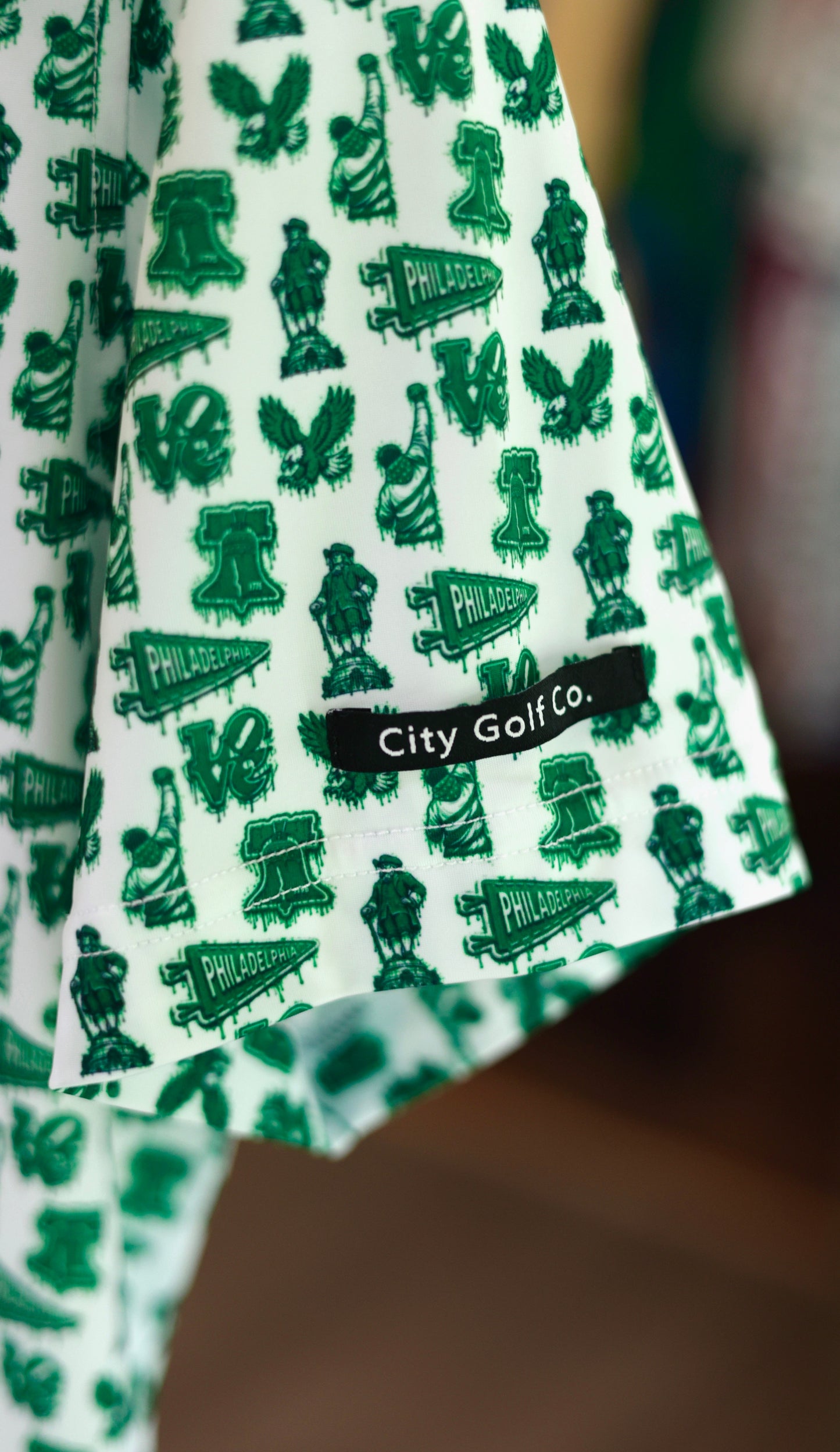 Close-up of The Bleeding Green Polo sleeve showcasing Philadelphia-inspired Kelly green graphics and City Golf Co. woven label.