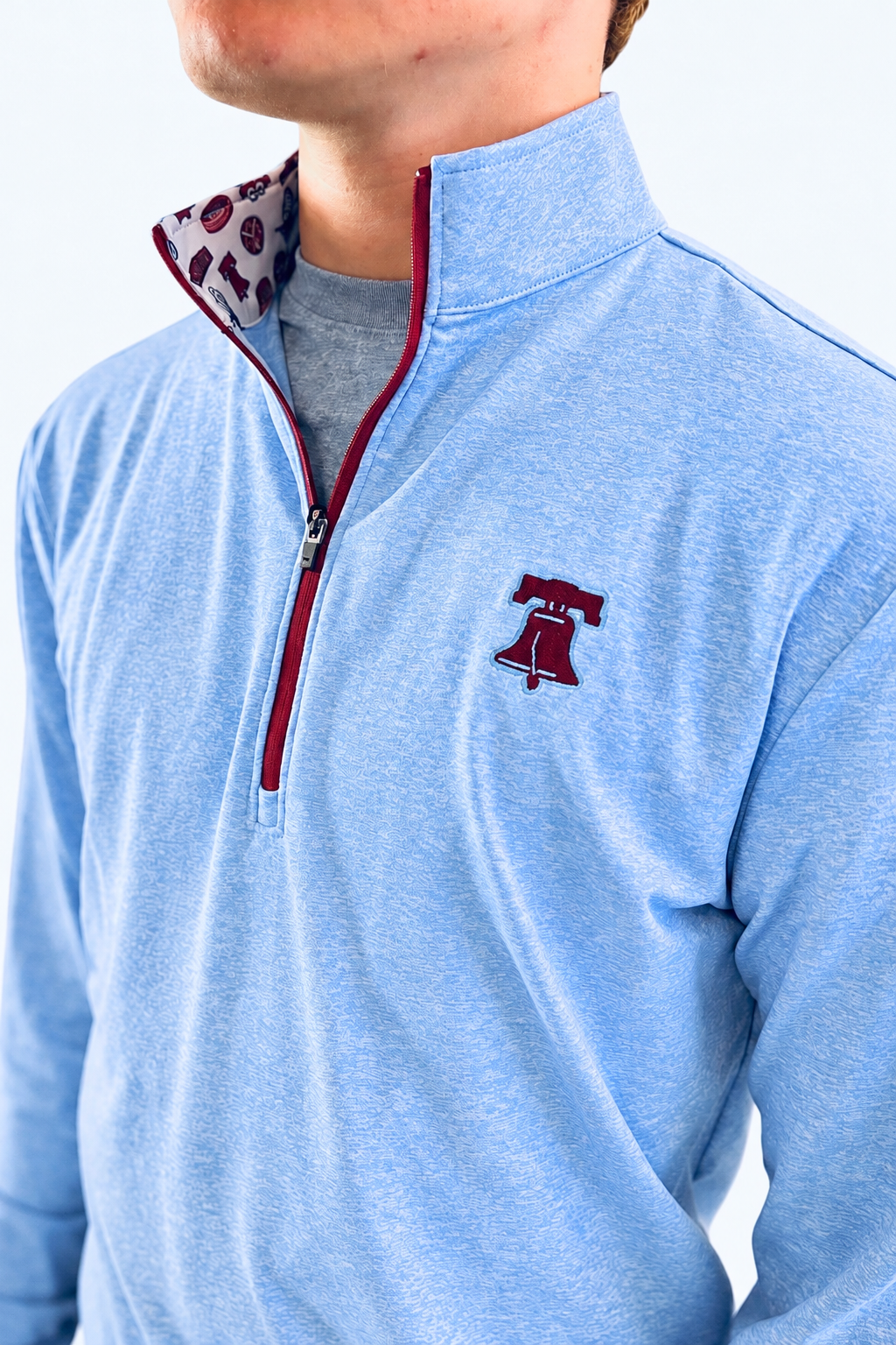 The Pattison Zip Up is a light blue heathered quarter-zip pullover with a maroon zipper and embroidered chest logo.