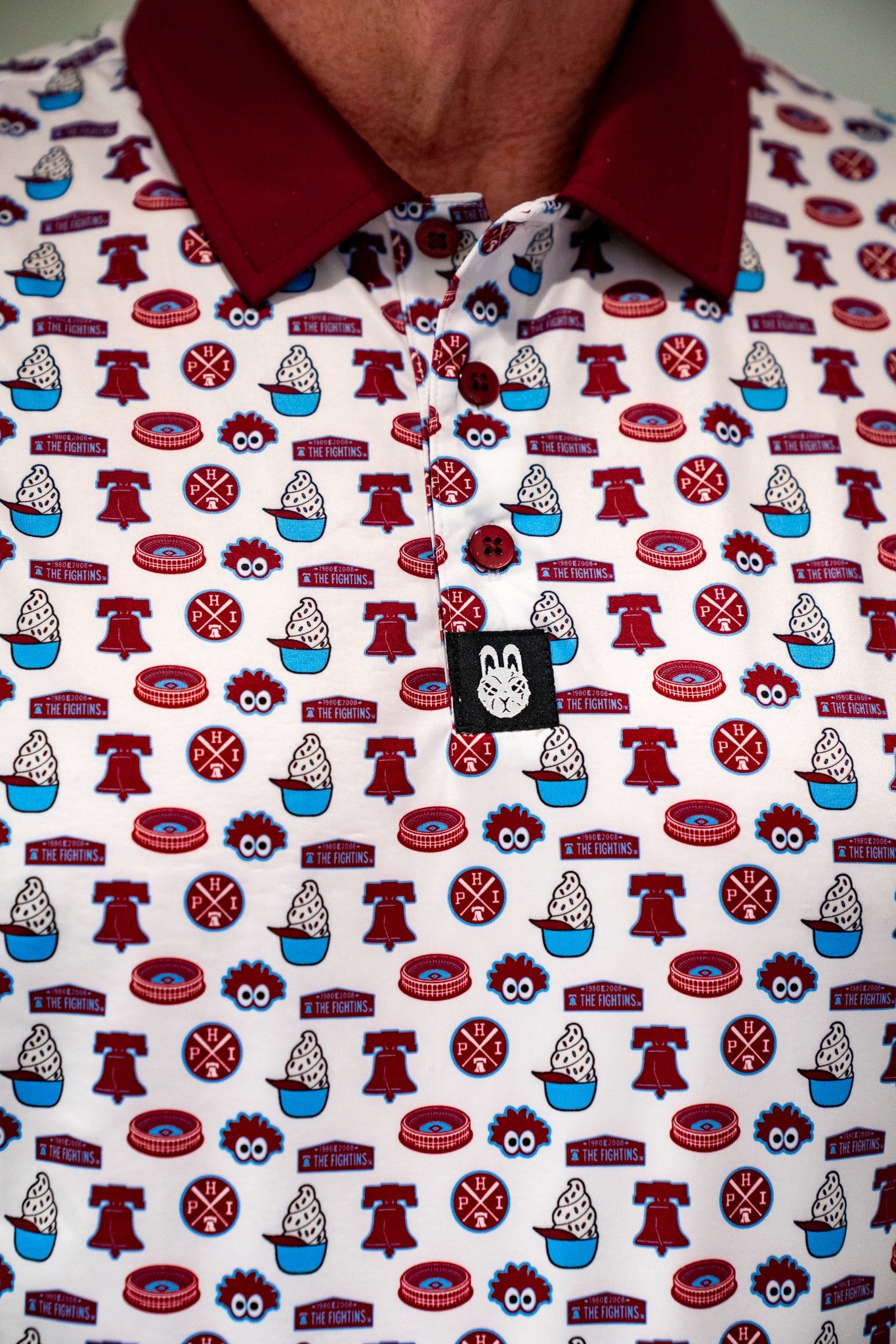Close-up of City Golf Collective Philadelphia-inspired golf polo featuring an all-over print design with retro ballpark-inspired artwork, maroon collar, and performance fabric construction.