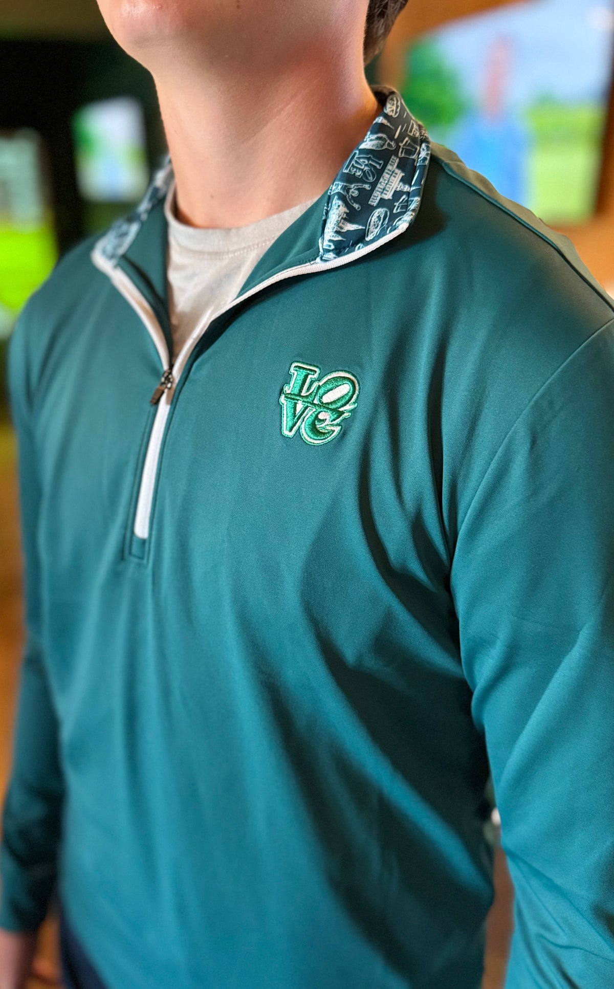 The Philly Heritage Zip Up is a teal athletic pullover with a quarter zip, patterned collar, and embroidered chest logo.
