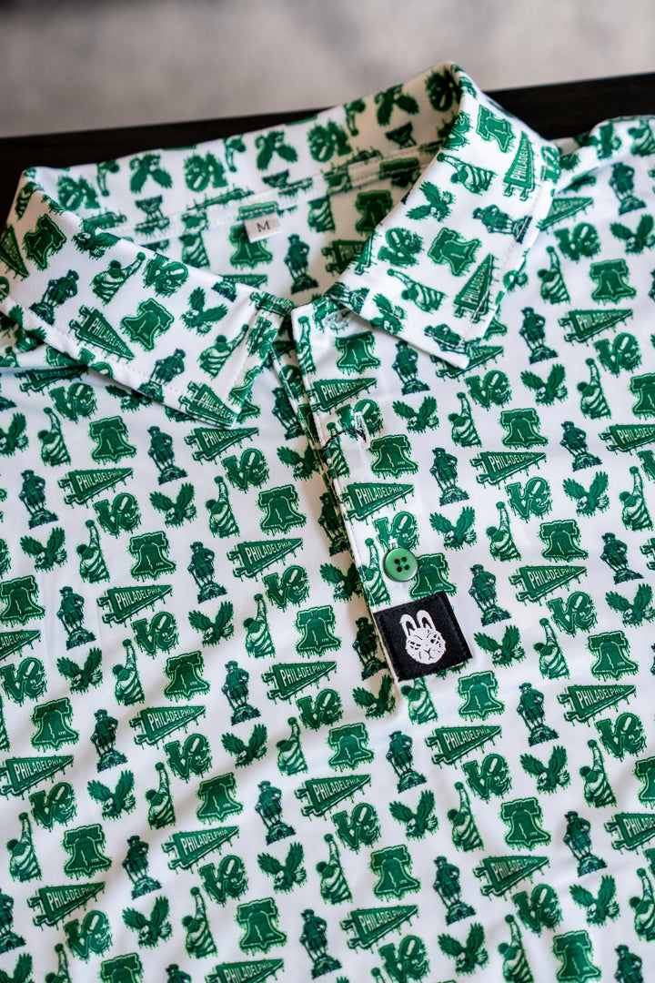 Close-up of white and green Philadelphia-themed performance golf polo featuring all-over city-inspired print and bunny logo tag