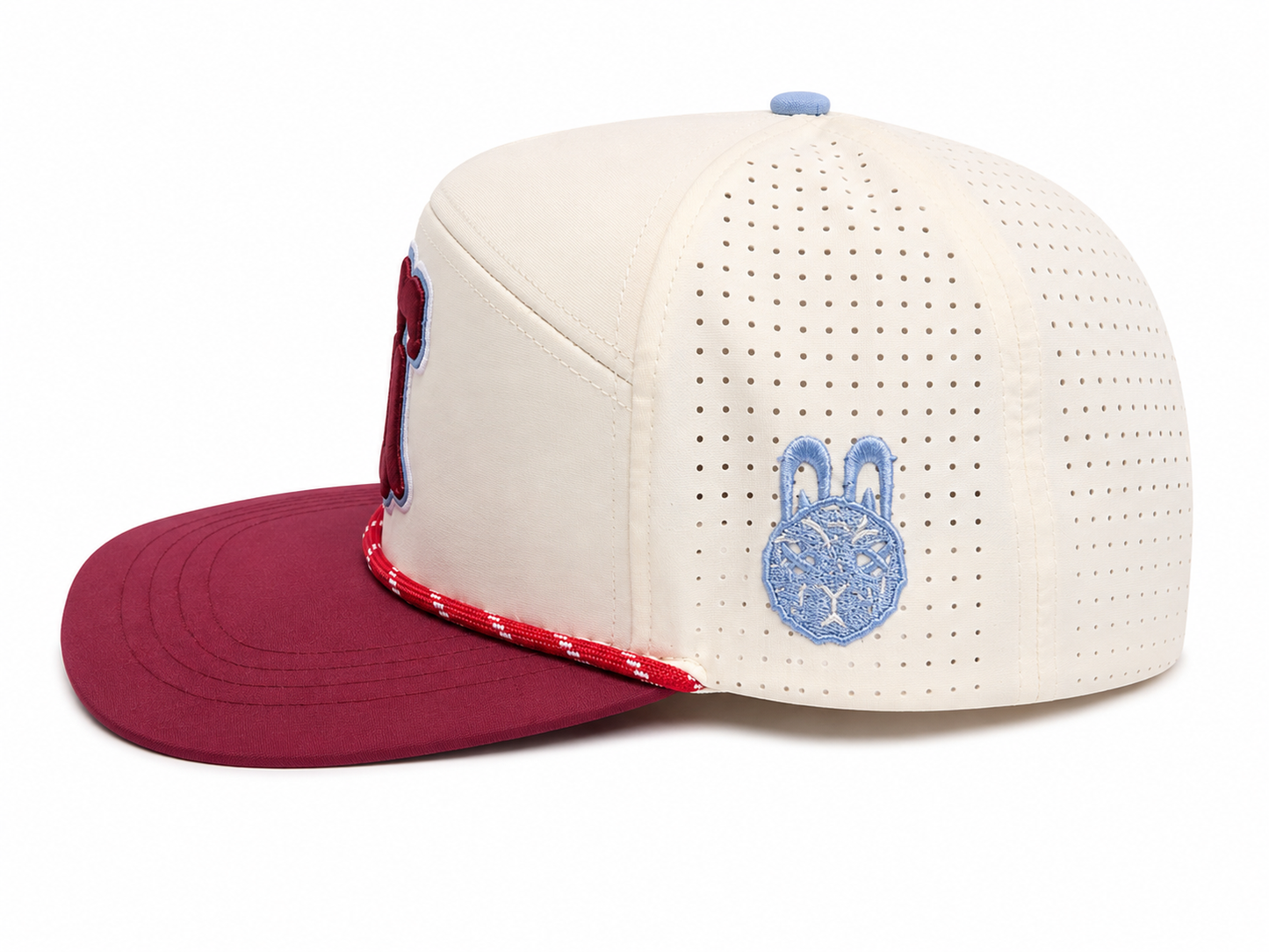 Side profile of the Ring the Bell Heritage Hat by City Golf Collective featuring cream performance fabric, maroon brim, rope detail, perforated side panels, and embroidered heritage artwork.