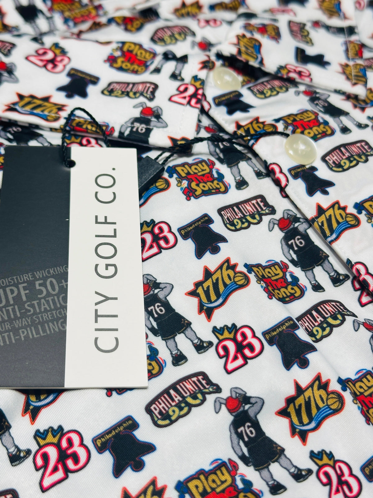 Close-up of Play the Song Polo performance fabric featuring colorful basketball-themed graphics, number 23, 1776 designs and City Golf Co. branding