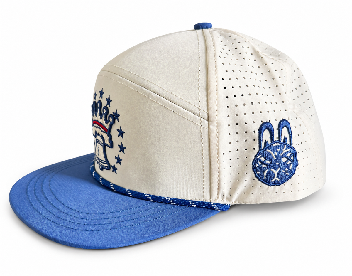 Side view: Cream and navy perforated performance hat with a square City Golf Collective bunny logo patch and breathable side panels.